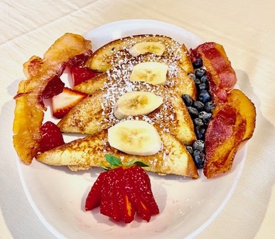 Plate of French toast with banana and strawberry slices and blueberries
