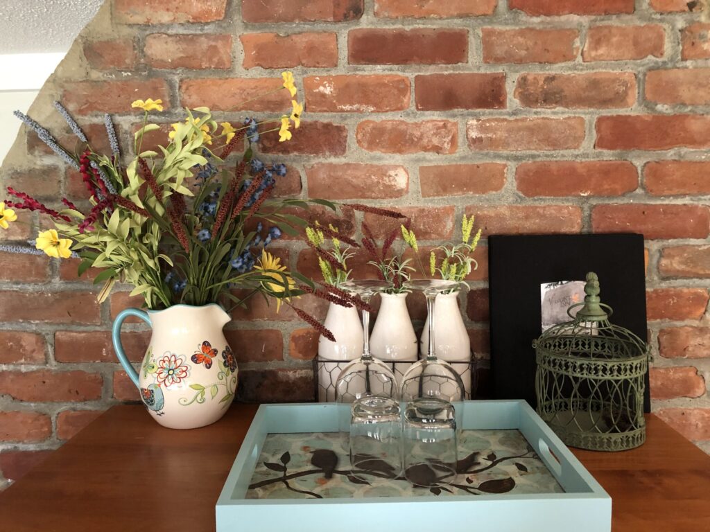 Vase and bottles with flowers and tray against brick background
