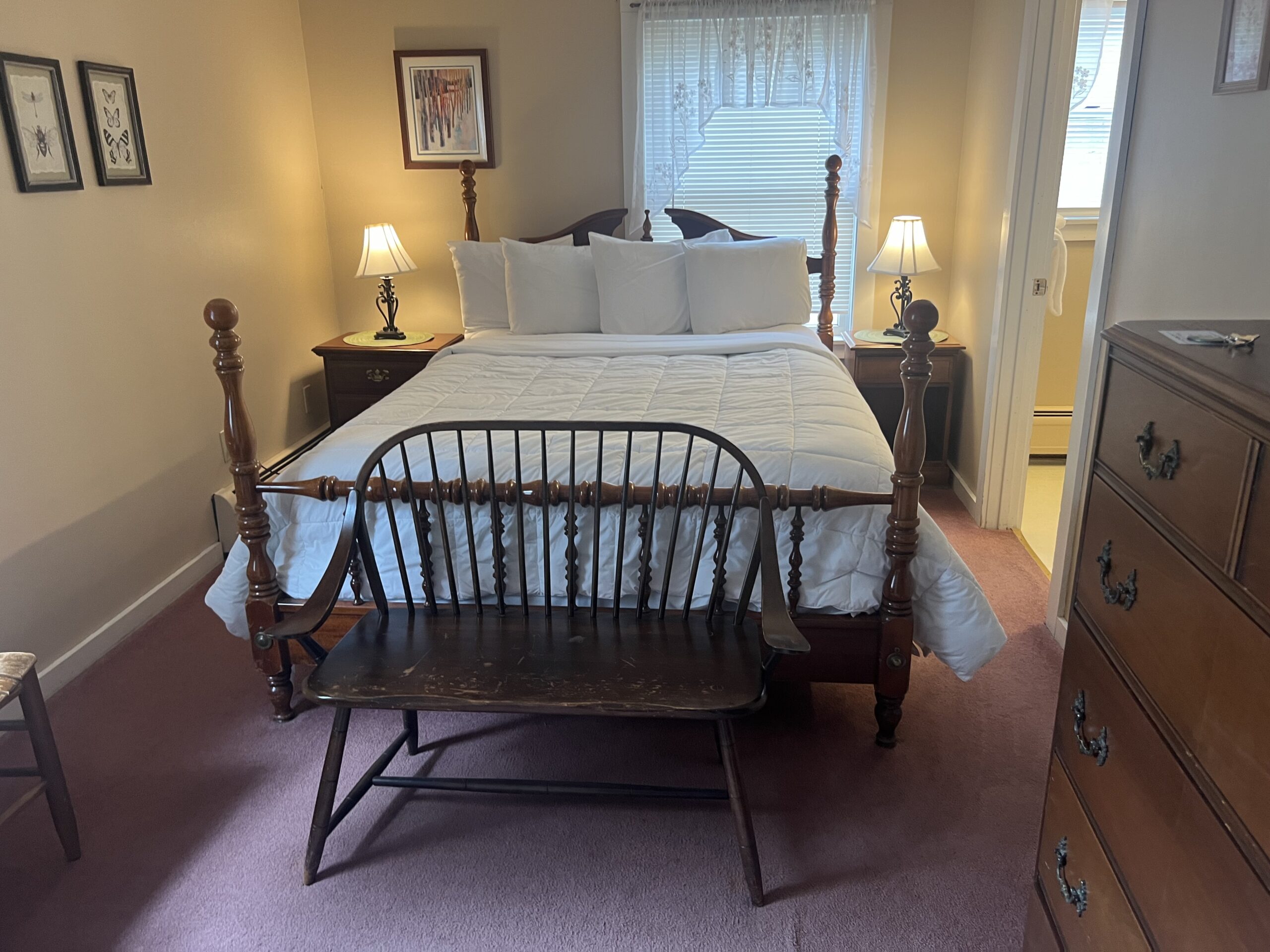 Bed with white comforter, maple headboard and footboard and wooden bench in front of bed.