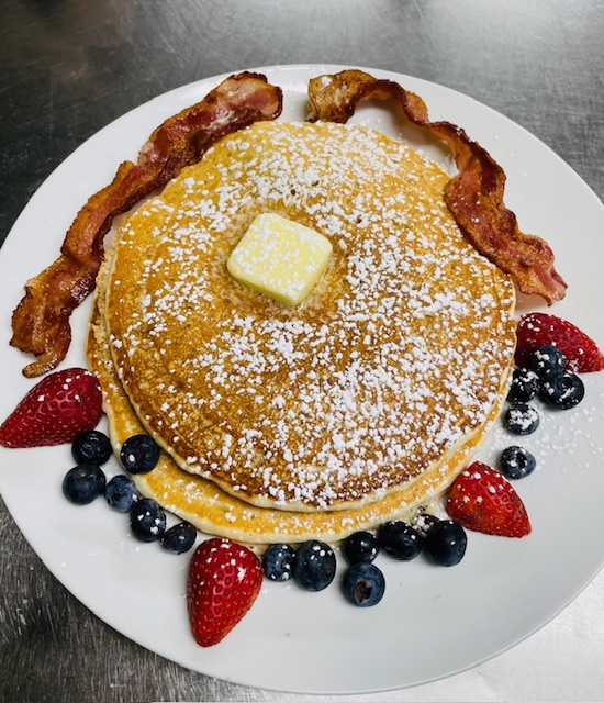 Plate of pancakes surround by berries and two. strips of. bacon.