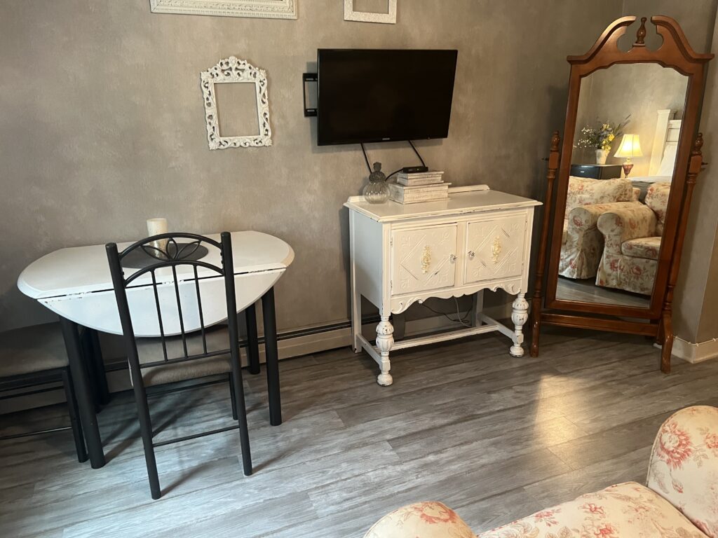 Small white table with black chairs, small white cabinet, and standing mirror